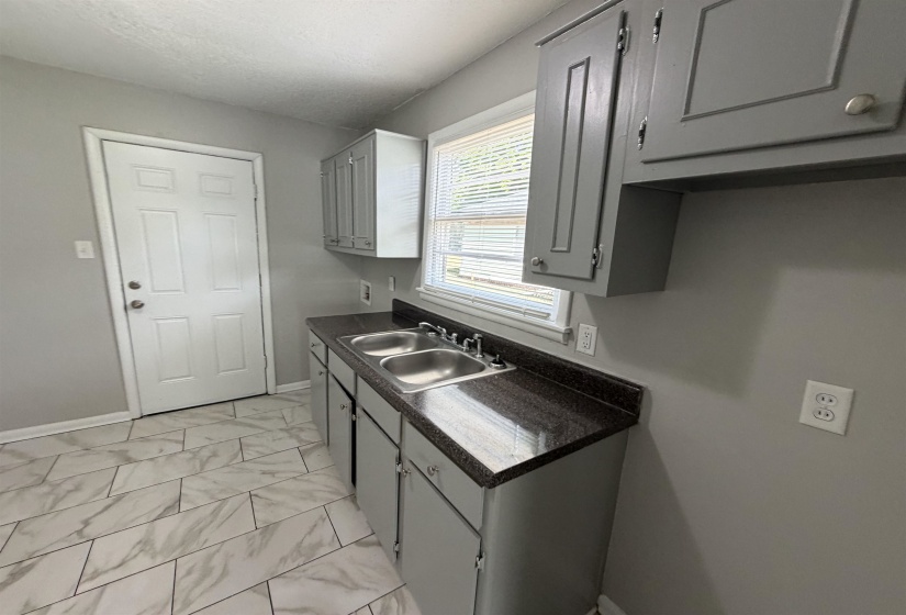 Kitchen featuring a double stainless steel sink, dark granite-style countertops, and light gray cabinetry
