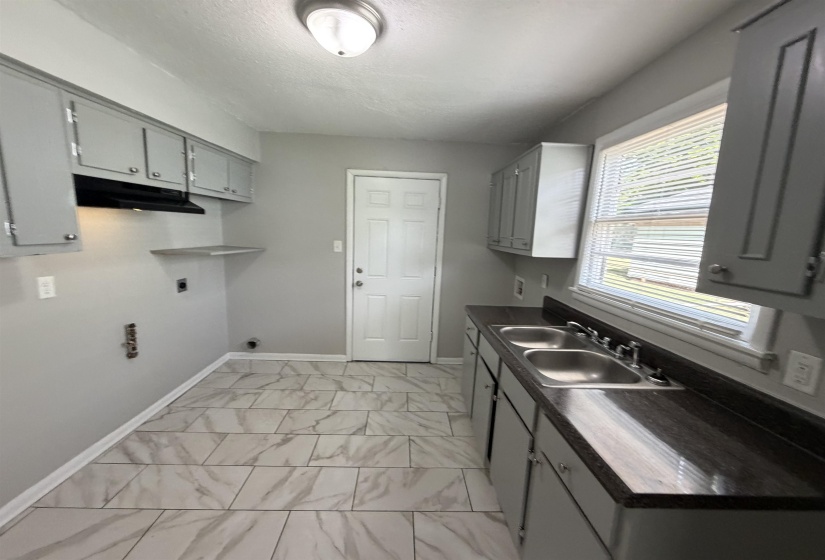 Kitchen area featuring grey cabinetry with silver-tone hardware, a double basin stainless steel sink, and dark countertops