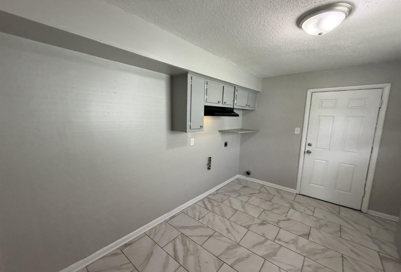 Utility area featuring gray upper cabinetry with a dark range hood, a wall-mounted shelf, and a white paneled door