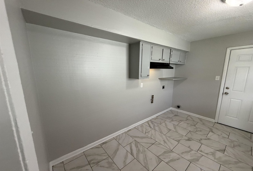 Utility area featuring marble-look tile flooring, gray painted walls, and white baseboards