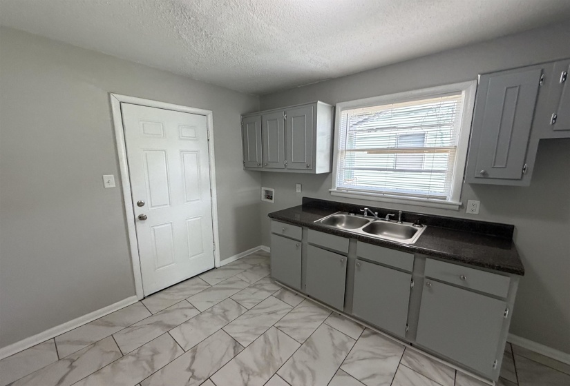 Kitchen area featuring gray cabinetry, dark countertops, a double-basin stainless steel sink, and light-toned tile flooring