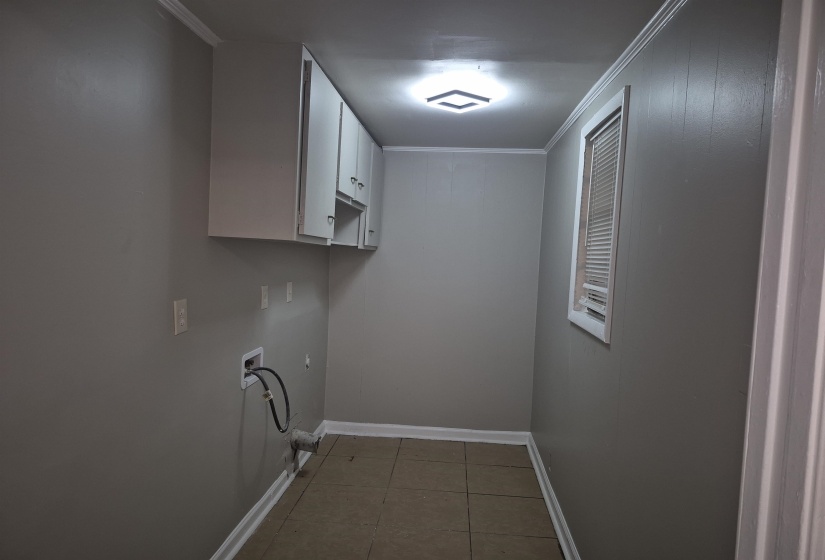 Dedicated utility area featuring overhead white cabinetry, tile flooring, and a single window with blinds
