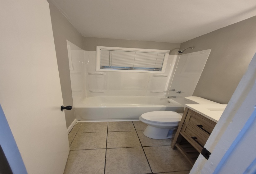 Bathroom featuring a full tub and shower combination with a window, contemporary vanity with a white countertop, modern toilet, and neutral-toned tile flooring