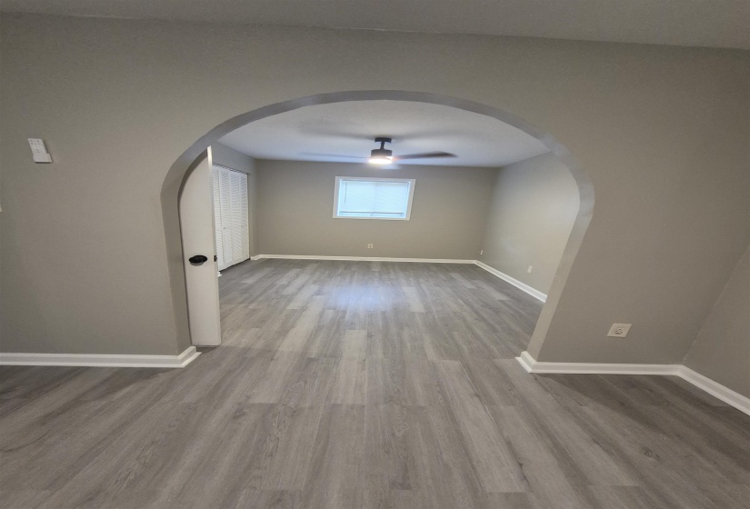 Spacious room featuring wood-finish flooring, an arched entryway, a ceiling fan, a window with blinds, and white trim
