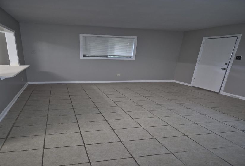 Square tile flooring, neutral gray wall tones, white trim, a single window with blinds, and an interior door