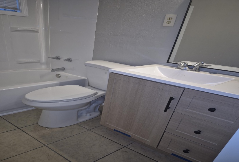 Bathroom featuring a light wood-finish vanity with a white countertop and integrated sink, a full-size mirror with a dark frame, a white toilet, and a white bathtub with a shower surround