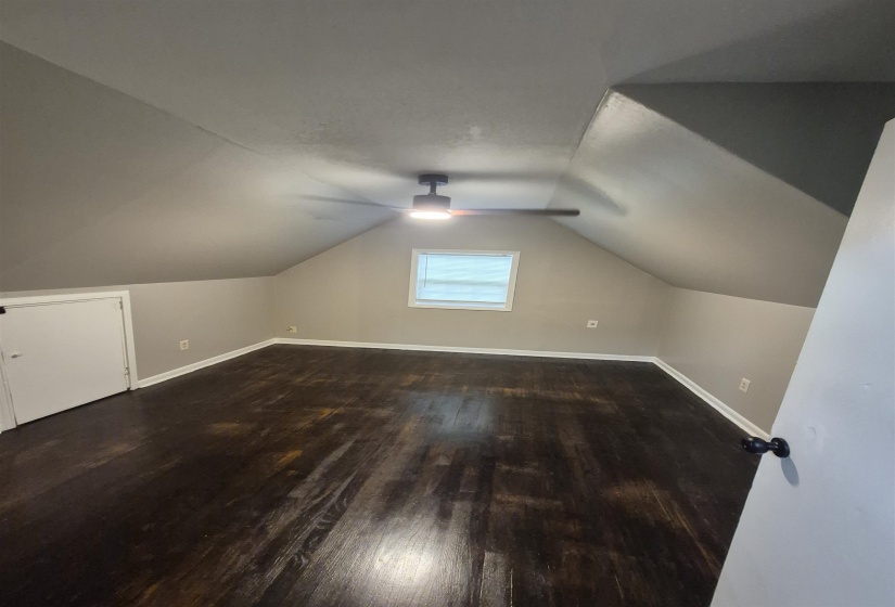 Attic room featuring dark wood-finish flooring, a contemporary ceiling fan with integrated lighting, and sloped ceilings