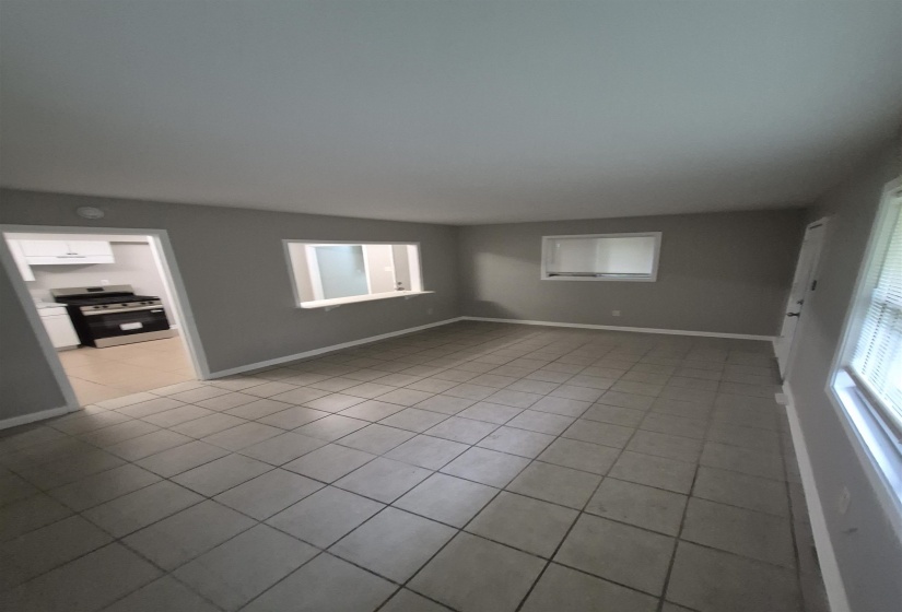 Neutral-toned tile flooring extends throughout this expansive living area, featuring a pass-through window to the kitchen