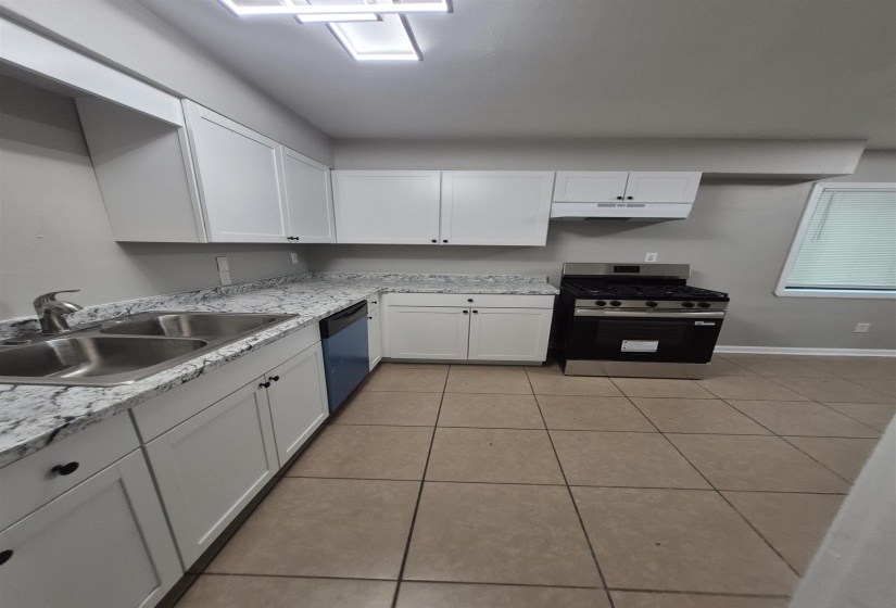Kitchen featuring white shaker-style cabinetry, a stainless steel double basin sink, a black stainless steel range, a built-in dishwasher, and granite-style countertops