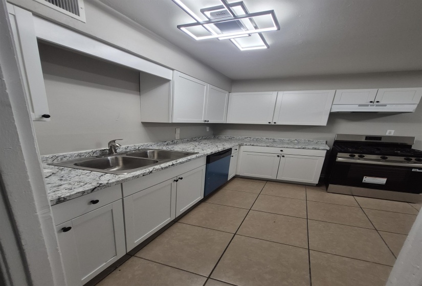Kitchen featuring white shaker-style cabinetry, a stainless steel double basin sink with an extendable faucet, and light-toned mottled countertops