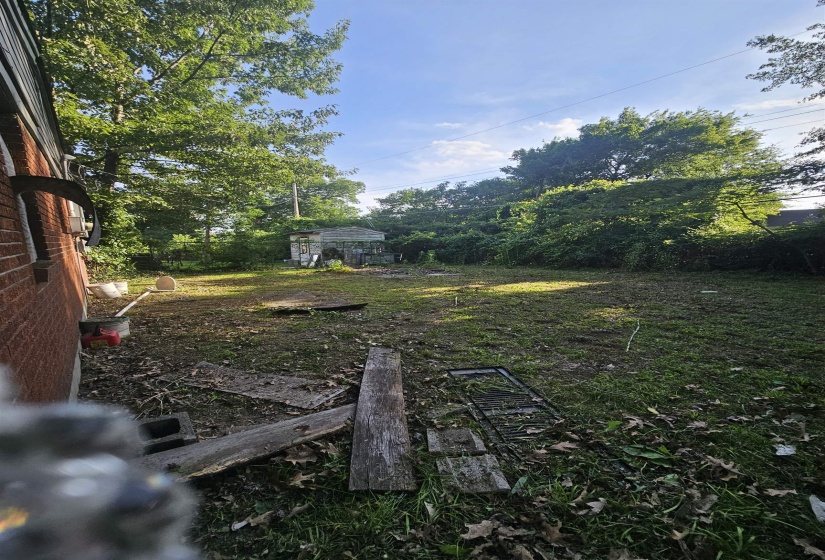 Expansive backyard area featuring a detached storage structure, mature trees, and a brick exterior wall
