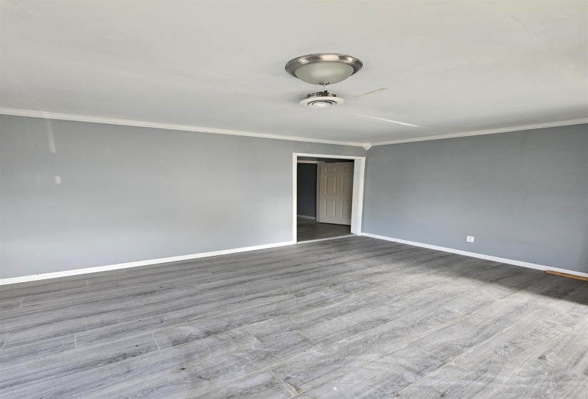 Spacious room featuring gray walls, wood-finish flooring, white crown molding, a ceiling fan with integrated lighting, and a white interior door