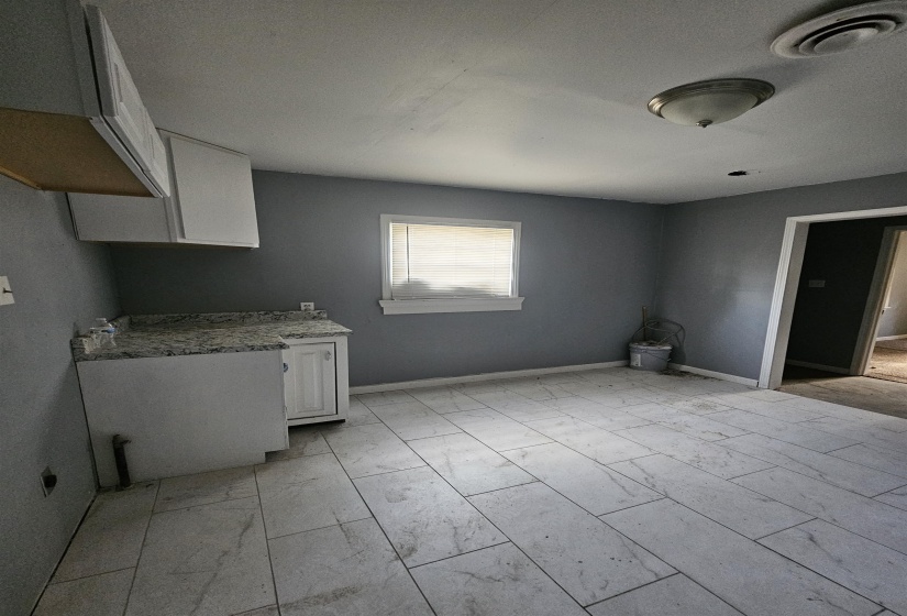 Kitchen space featuring grey wall paint, light-toned rectangular tile flooring, and a window with blinds