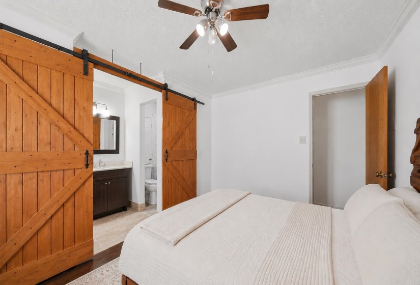 Primary bedroom with existing wood flooring, inluding custom barn doors, offering separation from primary ensuite, closet, and shower. Some features are AI-enhanced.