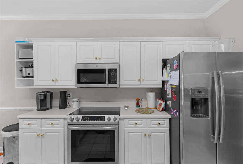 Kitchen featuring white shaker-style cabinetry, stainless steel appliances, a built-in microwave, white countertops, and crown molding