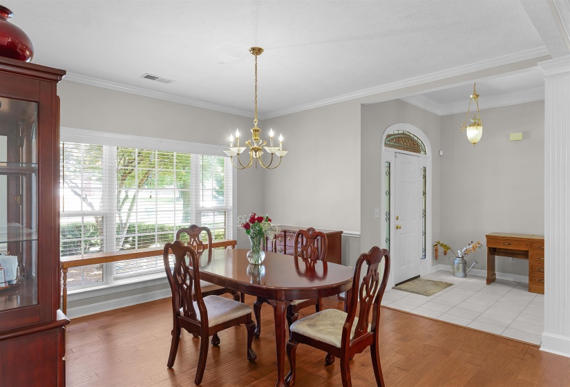 Dining area featuring hardwood-finish flooring, a large window with horizontal blinds, and a brass chandelier