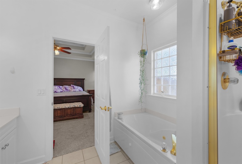 Bathroom featuring a white built-in soaking tub, a privacy block window, and a glass-enclosed shower with gold-tone hardware