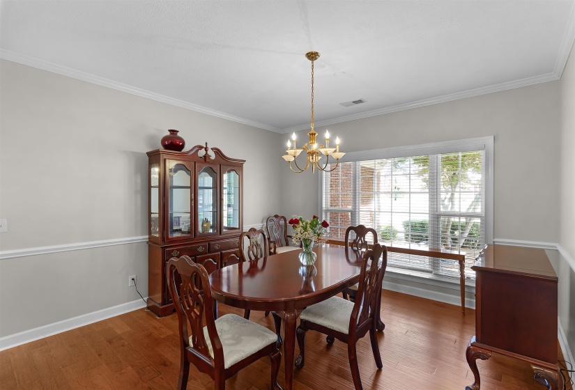 Dining area featuring wood-finish flooring, a large window with horizontal blinds, and a brass-tone chandelier