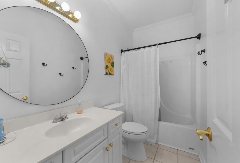 Bathroom featuring a white vanity with gold-tone hardware, a circular mirror, and a full bathtub with a shower enclosure