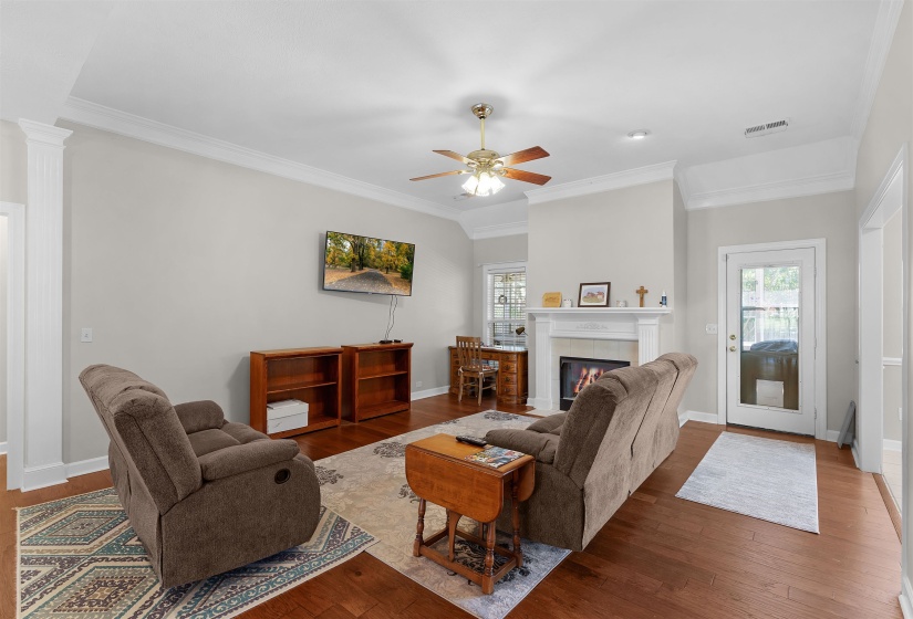 Spacious living area featuring wood-finish flooring, a white mantel fireplace, tray ceiling, and crown molding
