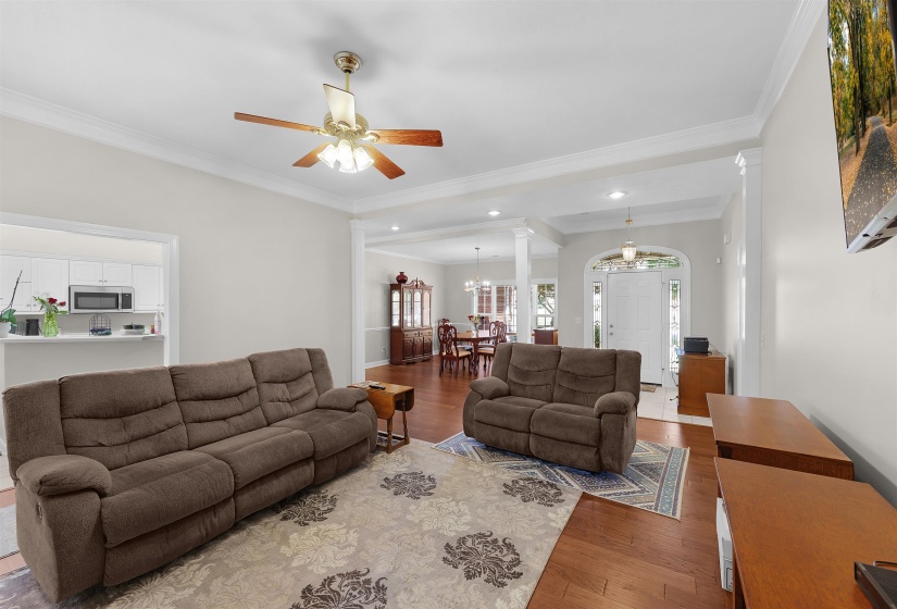 Living area featuring wood-finish flooring, crown molding, and a ceiling fan with integrated lighting