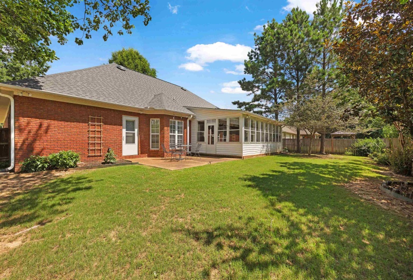 Expansive backyard featuring a manicured lawn, established landscaping, and a sunroom extension