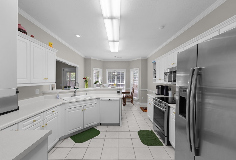Kitchen featuring white cabinetry with gold-finish hardware, stainless steel appliances, white tile flooring, and light-tone countertops