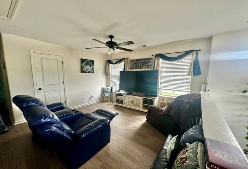 Living area featuring wood-finish flooring, a ceiling fan with integrated lighting, and white horizontal blinds