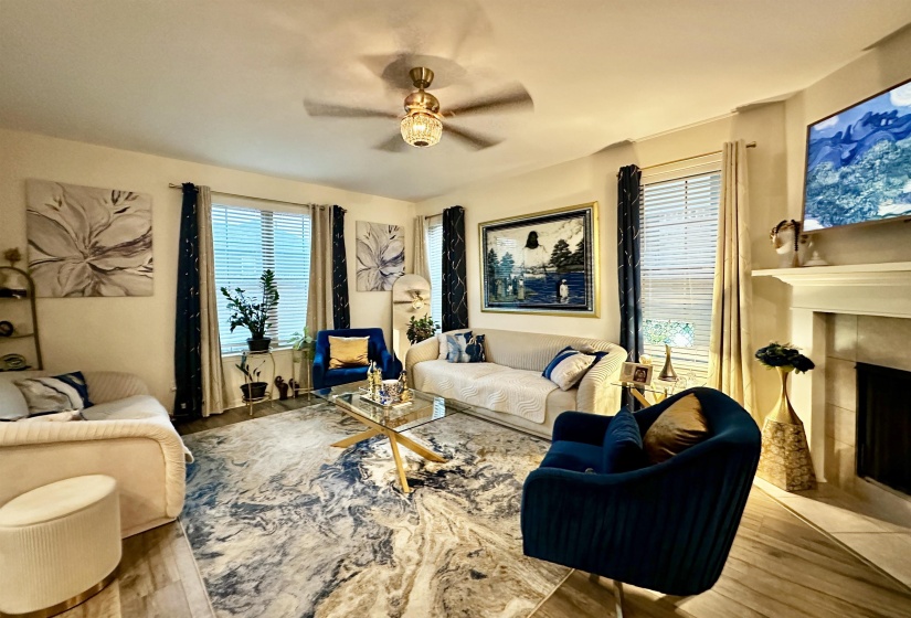 Living room featuring wood-finish flooring, a ceiling fan with integrated lighting, and multiple windows with blinds