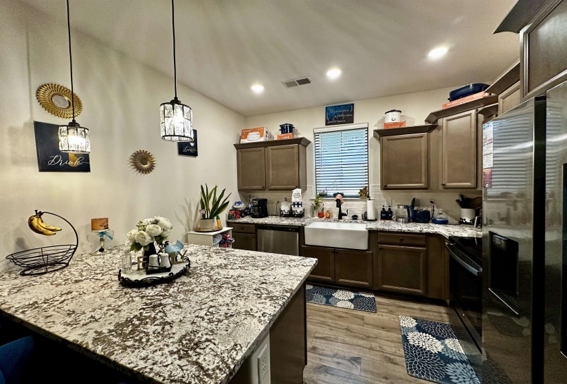 Kitchen featuring an oversized granite-finish island, dark wood-finish cabinetry, wood-finish flooring, stainless steel appliances, and a farmhouse sink