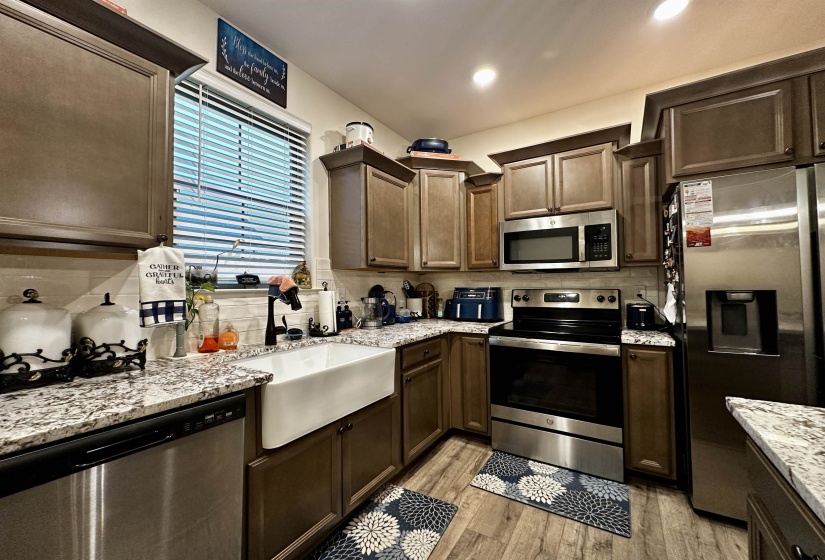 Kitchen featuring granite countertops, a farmhouse sink, stainless steel appliances, wood-finish flooring, and shaker-style cabinetry
