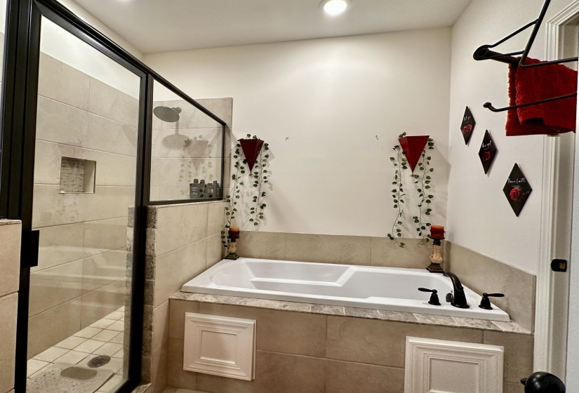 Built-in soaking tub with dark bronze fixtures set within a tiled surround, alongside a glass-enclosed shower featuring a tiled niche and a rain-style showerhead