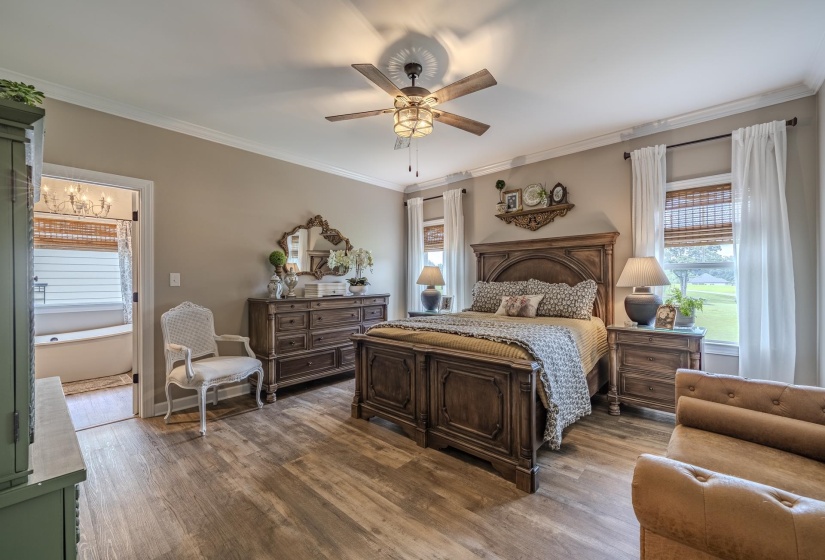 Spacious bedroom featuring wood-finish flooring, two windows with woven blinds and white drapes, and a ceiling fan with integrated lighting