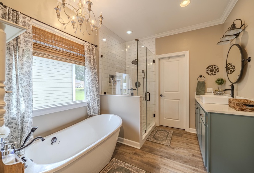 Bathroom featuring a freestanding soaking tub, a frameless glass shower enclosure with subway tile surround, a single vanity with a rectangular vessel sink and dark-toned cabinetry, wood-finish flooring, and a chandelier light fixture