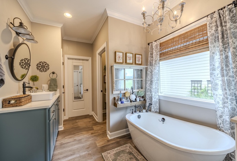 Freestanding soaking tub with a large window, complemented by wood-finish flooring
