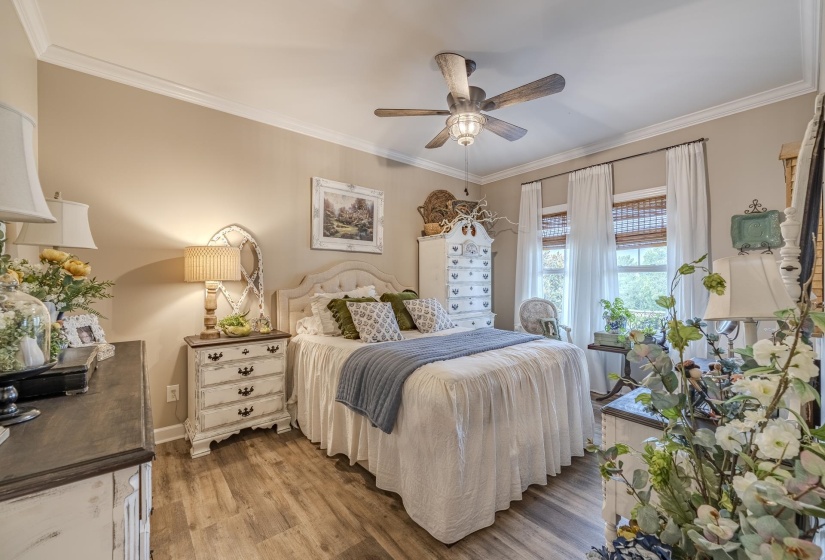 Warm bedroom featuring light wood-finish flooring, a ceiling fan with light, and crown molding
