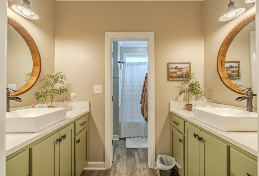 Dual vanity bathroom featuring vessel sinks, light green cabinetry, white countertops, and wood-finish flooring