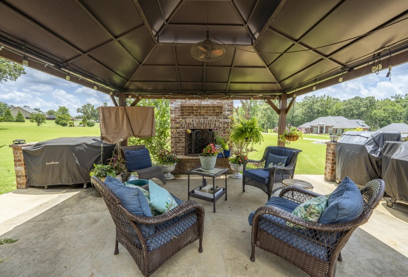 Spacious covered patio featuring a brick fireplace, built-in brick base, and a ceiling fan