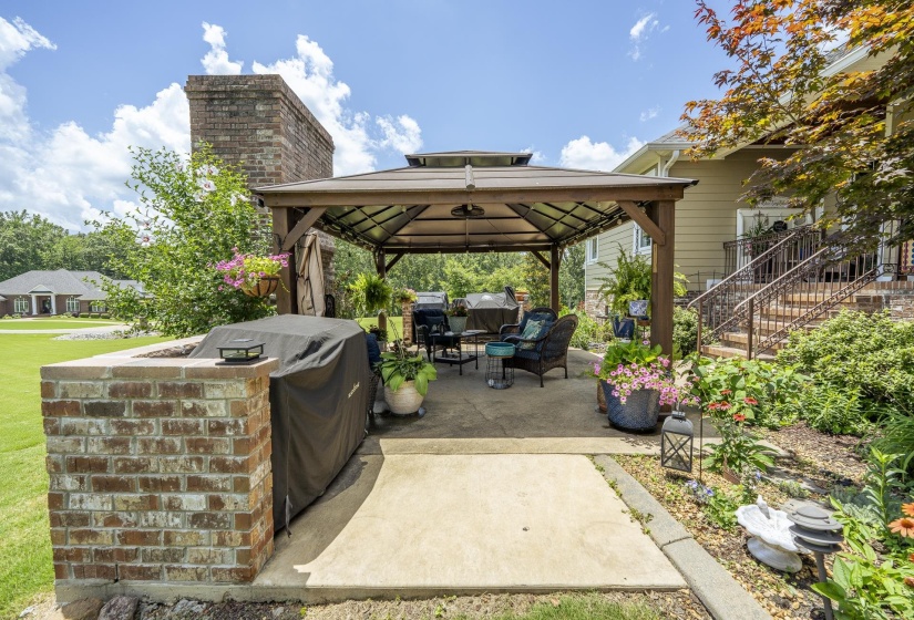 Expansive outdoor patio featuring a covered gazebo, brick-built outdoor kitchen with a grill, and a terraced garden area with established landscaping