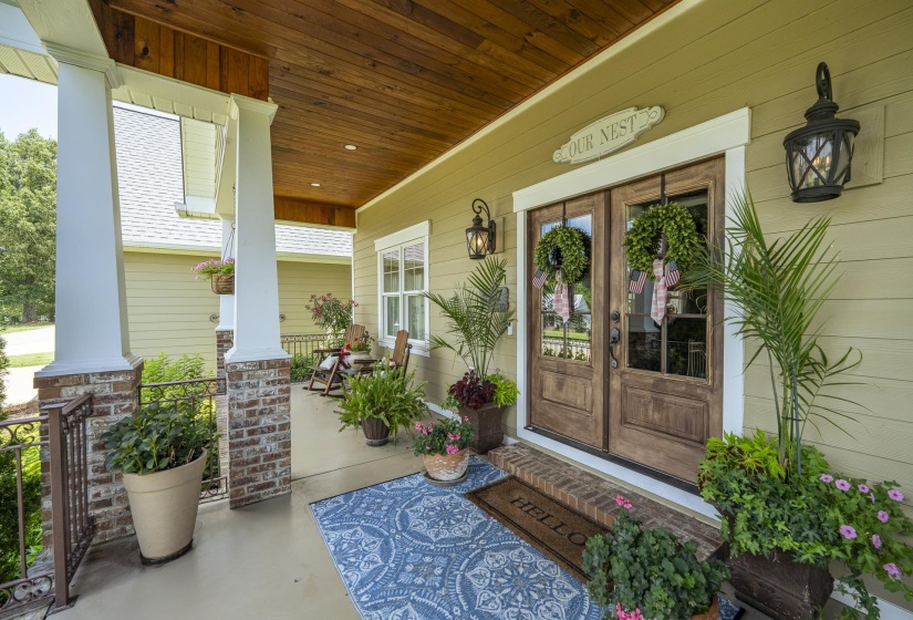 Covered front porch featuring a wood-panel ceiling, brick and white column bases, and decorative wrought iron railing