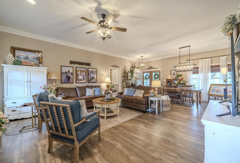 Open-concept living and dining area featuring wood-finish flooring, crown molding, and a neutral wall palette