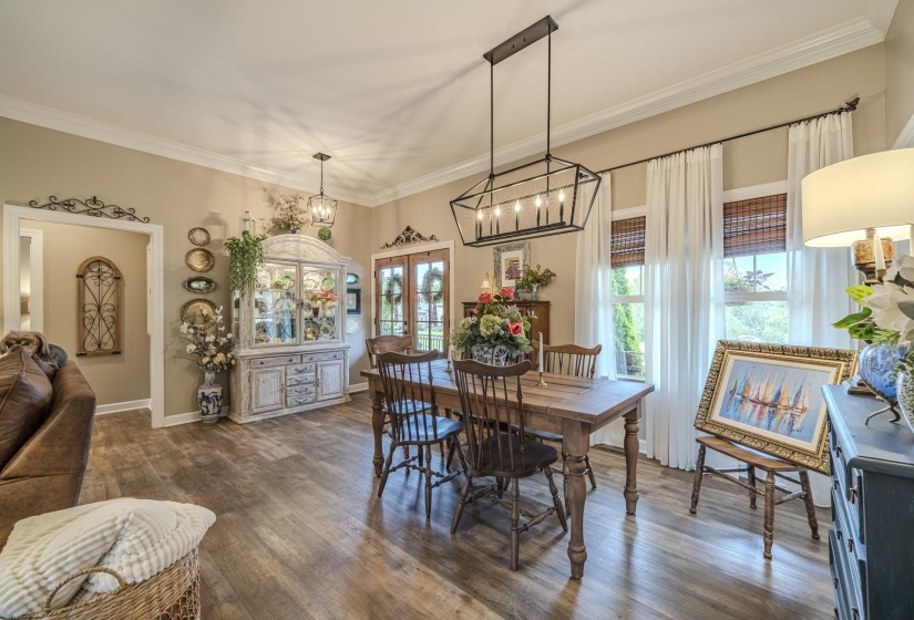 Spacious dining area featuring wood-finish flooring, a linear chandelier, crown molding, double windows with window treatments, and an arched doorway
