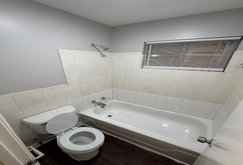 Bathroom with shower / washtub combination, wood finished floors, a textured ceiling, and tile walls