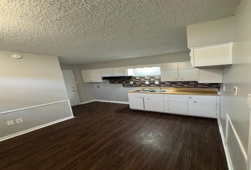 Kitchen featuring light countertops, white cabinetry, dark wood-style floors, decorative backsplash, and a textured ceiling