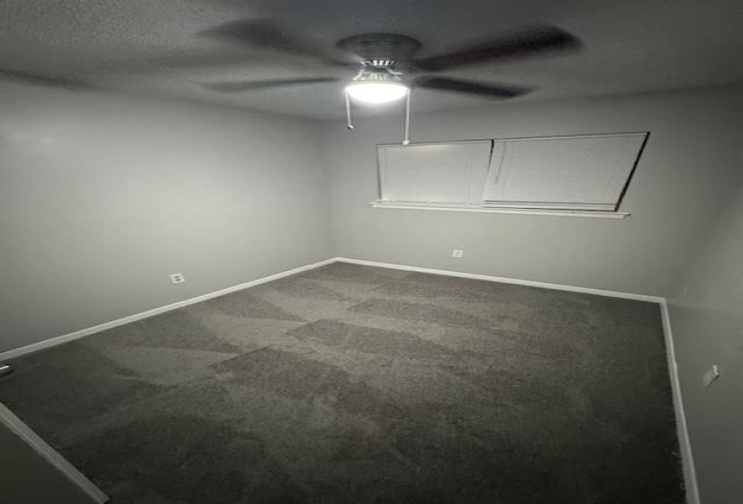Unfurnished room with dark carpet, a textured ceiling, and a ceiling fan