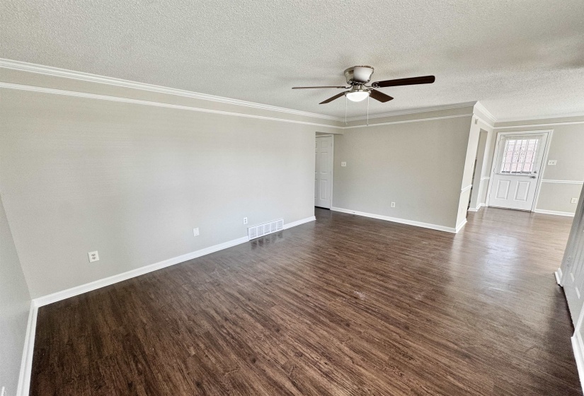 Empty room featuring dark wood-type flooring, a textured ceiling, ornamental molding, and a ceiling fan