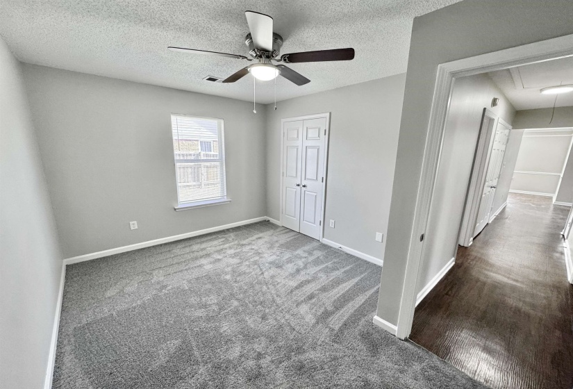 Unfurnished bedroom featuring attic access, a textured ceiling, carpet flooring, ceiling fan, and a closet