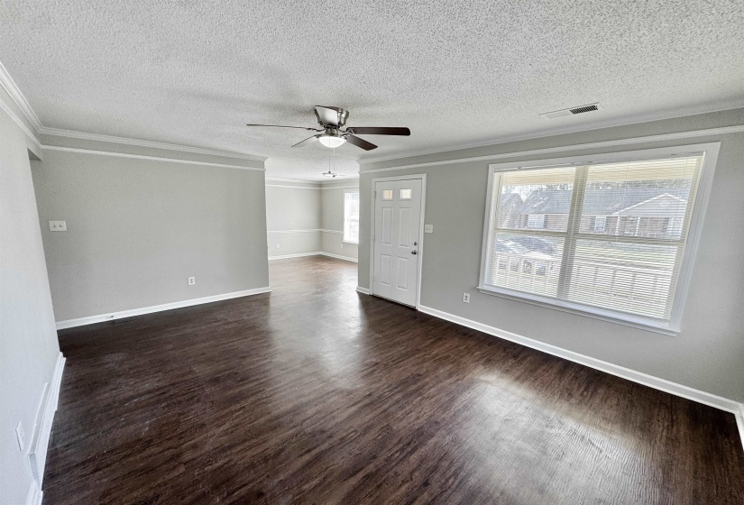 Unfurnished living room featuring ornamental molding, a textured ceiling, dark wood-style flooring, and a ceiling fan