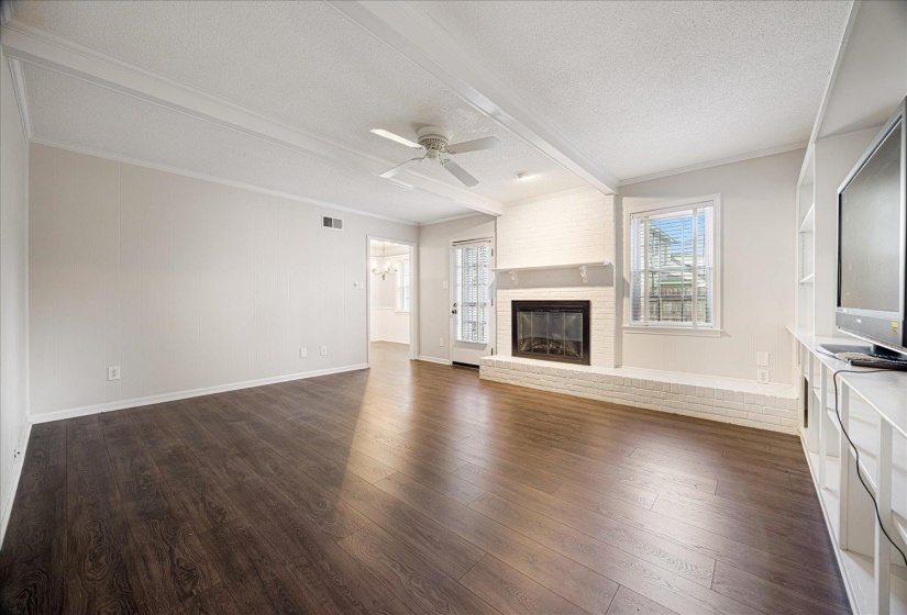 Unfurnished living room featuring beam ceiling, a textured ceiling, dark wood-style flooring, a brick fireplace, and ornamental molding