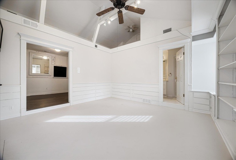 Spare room featuring high vaulted ceiling, ceiling fan, and wainscoting, with private bathroom
